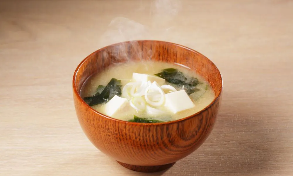 Steaming miso soup with tofu, seaweed, and green onions in a wooden bowl at Blue Coast Asian Cuisine, a Asian restaurant in Davenport